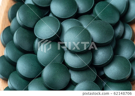 Vitamin and mineral supplements for vegetarians spirulina in tablets in a wooden spoon, close-up. Vitamin and mineral supplements for vegetarians spirulina in tablets in a wooden spoon, close-up. 62148706