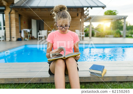Young girl in glasses near the pool with a pile of books, reading book. Education, summer, knowledge 62150265