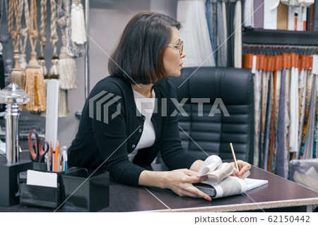Workplace female designer, business woman in glasses with notebook pen and sample of fabric working in the office Workplace female designer, business woman in glasses with notebook pen and sample of fabric working in the office 62150442