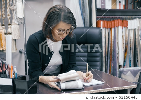 Workplace female designer, business woman in glasses with notebook pen and sample of fabric working in the office Workplace female designer, business woman in glasses with notebook pen and sample of fabric working in the office 62150443