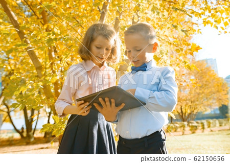 Two kids watching digital tablet, background autumn sunny park, golden hour 62150656