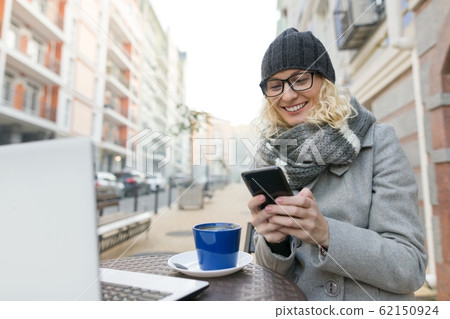 Young business woman in outdoor cafe with computer, mobile phone. Urban autumn background 62150924