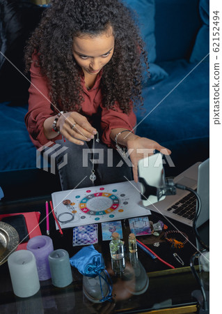 Focused young woman using a crystal pendulum Focused young woman using a crystal pendulum 62152494