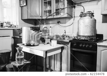 Old-fashioned moonshine machine for creating homemade strong alcohol in the kitchen. Process of distillation, general view. Story about an aged way of distilling moonshine at home. Monochrome effect 62154478