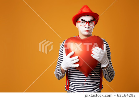 Close up mime in red hat and vest holds heart ball in his hands 62164292