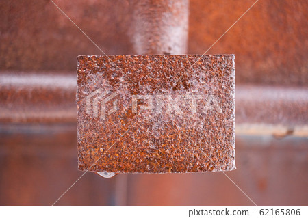 Wet rusty metal rectangular plate in middle of frame. Background blurred. Wet rusty metal rectangular plate in middle of frame. Background blurred. 62165806