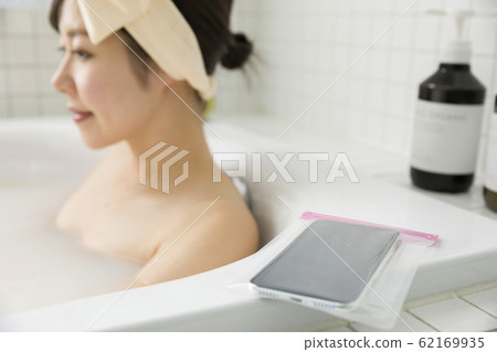 一名年輕女子將帶防水套的智能手機帶入浴室 62169935