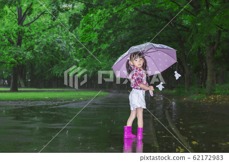 看有傘和微笑的一個女孩一個黑暗的多雨森林。 看有傘和微笑的一個女孩一個黑暗的多雨森林。 62172983