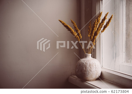 White textured hand-made ceramic vase with dry ears on windowsill 62173804