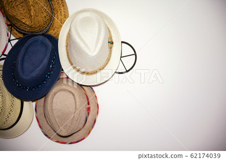 close up of many summer hat on a white wall. Straw Hats for summer hanging on white wall in hotel. Accessories and travel concept close up of many summer hat on a white wall. Straw Hats for summer hanging on white wall in hotel. Accessories and travel concept 62174039