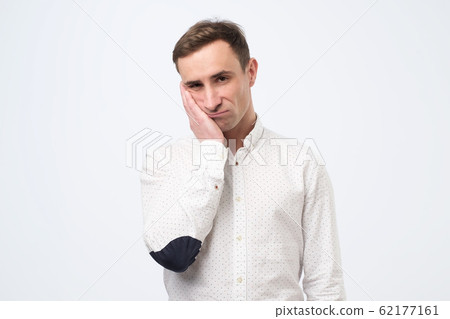 Very bored adult italian man holding hand on cheek looking tired and sick Very bored adult italian man holding hand on cheek looking tired and sick 62177161