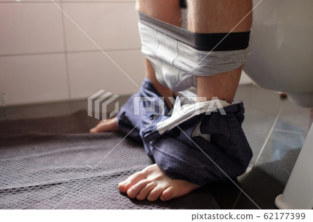 Man sitting in the restroom urinating having health problems. 62177399