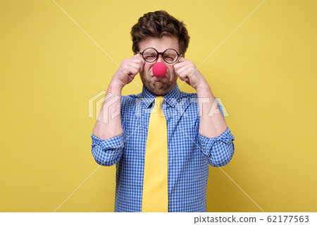 Sad caucasian man dressed as clown crying against a yellow background Sad caucasian man dressed as clown crying against a yellow background 62177563