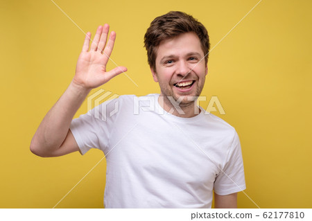 Young man dressed in white t-shirt saying hi or goodbye, waving his hand 62177810