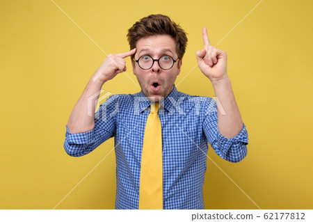 man in glasses yellow tie and blue shirt has intriguing expression pointing finger up having great idea looks happily man in glasses yellow tie and blue shirt has intriguing expression pointing finger up having great idea looks happily 62177812