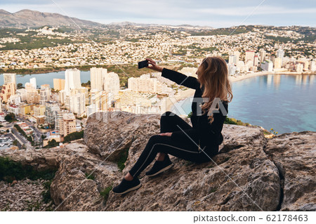 Woman seated on stone rock posing makes selfie 62178463