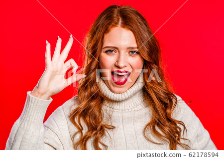 Positive girl making OK sign over red background and smiles to camera. Body language. Young woman in white winter sweater Positive girl making OK sign over red background and smiles to camera. Body language. Young woman in white winter sweater 62178594