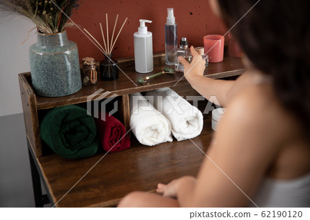 Young woman putting bottle of perfume on shelf Young woman putting bottle of perfume on shelf 62190120