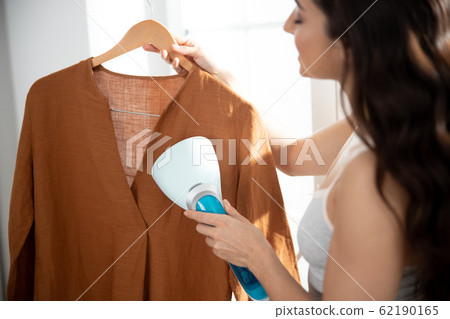 Young lady using clothes steamer to freshen up shirt 62190165