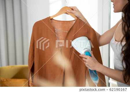 Young lady refreshing shirt with clothes steamer 62190167