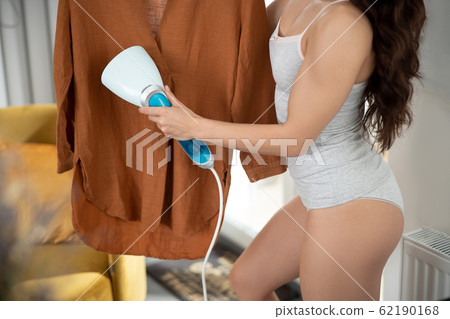 Young woman using electric handheld clothes steamer Young woman using electric handheld clothes steamer 62190168