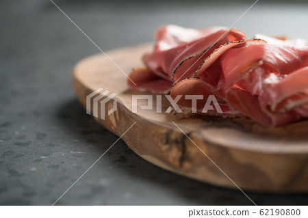 Sliced prosciutto ham on olive wood board 62190800