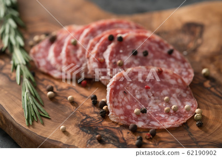 Sliced salame milano sausage on olive wood board with rosemary and pepper Sliced salame milano sausage on olive wood board with rosemary and pepper 62190902