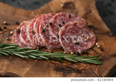 Sliced salame milano sausage on olive wood board with rosemary and pepper 62190904