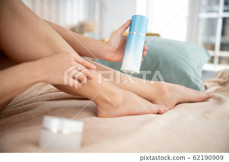 Lady holding cosmetic cream and touching leg Lady holding cosmetic cream and touching leg 62190909