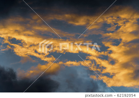 Golden fluffy clouds illuminated by disappearing rays at sunset and dark thunderclouds floating across sunny blue sky to change season weather Golden fluffy clouds illuminated by disappearing rays at sunset and dark thunderclouds floating across sunny blue sky to change season weather 62192054