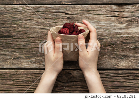 Home-made beet chips. Snacks are wrapped in a paper bag. Hand holds food bag. Handmade healthy vegetables chips 62193281