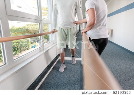 Therapist helping young man learning to walk again in rehabilitation Therapist helping young man learning to walk again in rehabilitation 62193593
