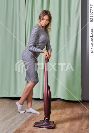 Slender girl uses cordless vertical vacuum cleaner 62197777