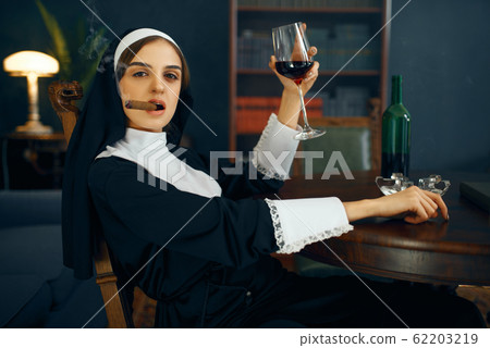 Nun in a cassock smokes cigare and drinks wine Nun in a cassock smokes cigare and drinks wine 62203219