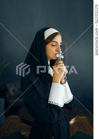 Young nun in a cassock prays crossed her arms Young nun in a cassock prays crossed her arms 62203229