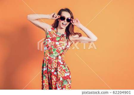 Girl in floral dress emotionally poses on the orange background Girl in floral dress emotionally poses on the orange background 62204901