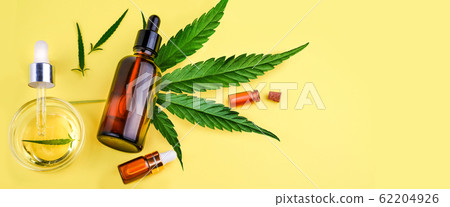 Glass bottles with CBD oil, THC tincture and hemp leaves on a yellow background. Flat lay, minimalism. Cosmetics CBD hemp oil. Banner 62204926