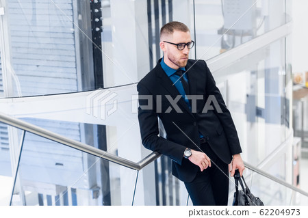 Elegant young adult man standing on stairs with bag in hand. He looking aside. 62204973