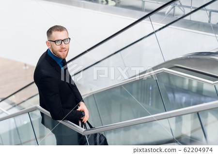 Elegant young adult man standing on stairs with bag in hand. He looking aside. 62204974