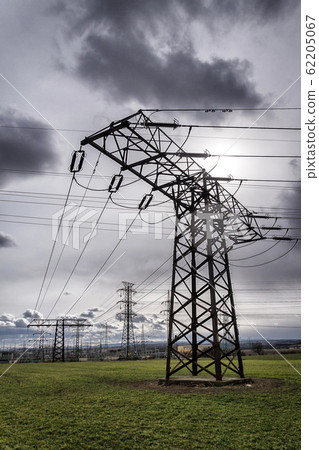 Sun hidden behind dramatic clouds and electricity pylons conducting current from distribution power station, solar renewable energy and grid stability concept, copy space Sun hidden behind dramatic clouds and electricity pylons conducting current from distribution power station, solar renewable energy and grid stability concept, copy space 62205067