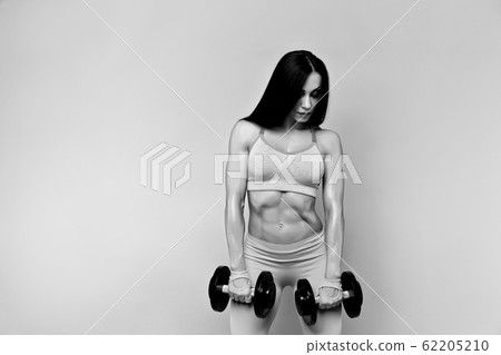 Muscular woman working out with dumbbells. Isolated. Gray Muscular woman working out with dumbbells. Isolated. Gray 62205210