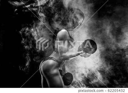 Muscular unrecognizable brunette in bikini doing exercise on biceps with dumbbells in smoke Muscular unrecognizable brunette in bikini doing exercise on biceps with dumbbells in smoke 62205432