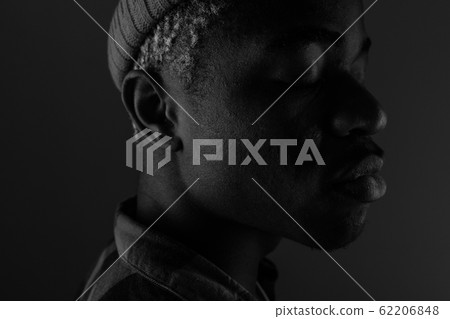 Close-up portrait of a dark-skinned guy with big lips looking sideways in black and white light 62206848