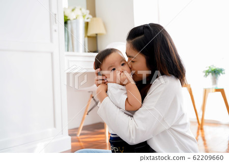 Asian young adult mother kissing joyful son in living room. Asian young adult mother kissing joyful son in living room. 62209660