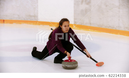 Curling - a woman pushes off on the ice field with a granite stone holding a brush Curling - a woman pushes off on the ice field with a granite stone holding a brush 62214338