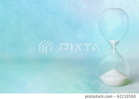 Time. An hourglass with flowing sand on a pastel blue background with a place for text, toned image Time. An hourglass with flowing sand on a pastel blue background with a place for text, toned image 62218508