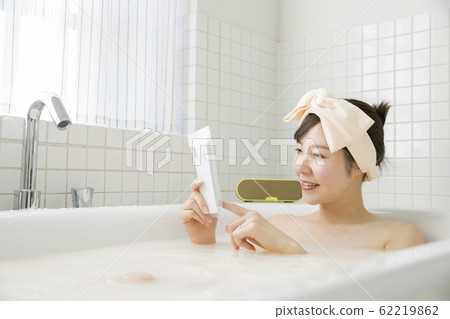 Young woman watching smartphone by putting smartphone in waterproof case in bathroom Young woman watching smartphone by putting smartphone in waterproof case in bathroom 62219862