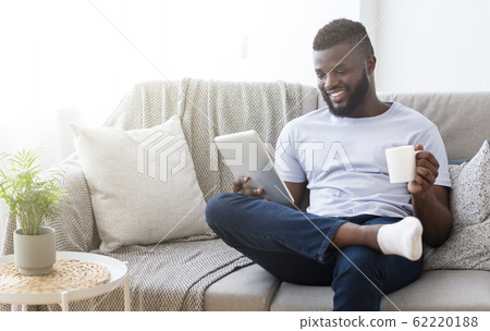 Cheerful black man reading news on digital tablet with coffee Cheerful black man reading news on digital tablet with coffee 62220188