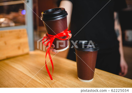 A woman holds a plastic glass of coffee into the camera 62225034