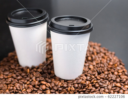 Two White cups of hot coffee on a dark background. Coffee beans background. Vintage style, food banner. Coffee to go in a paper cup, selective focus 62227106